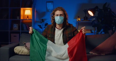 Responsible young man in protective mask holding italian flag while sitting on Stock Footage 127416779