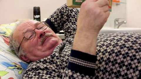 Rest in hosp bed old man looks at us and read the book Stock Footage 81836466