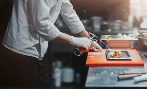 Restaurant Chef cook preparing salmon filet flambe in open kitchen. Stock Photos