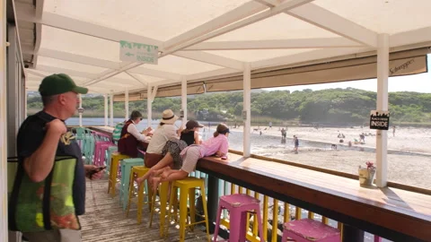 Restaurant-goers with drinks at restaurant overlooking Onrus beach and lagoon Stock Footage 319750108