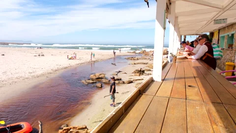 Restaurant-goers at Milk On The Beach overlooking Onrus lagoon and beachgoers Stock Footage 319512465