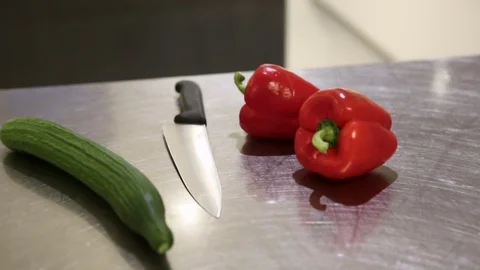 Restaurant kitchen table with a cucumber, bell peppers and a knife Stock Footage 82076699