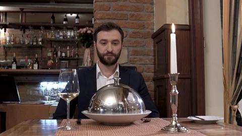Restaurant visitor is sitting in front of the camera. Waiter opens cloche Video stock 89043435