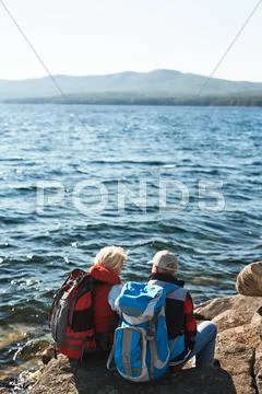 Restful senior couple sitting on stones by water during trip Stock Photos