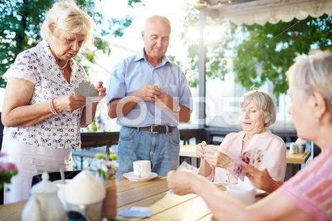Restful seniors playing cards in outdoor cafe at leisure Stock Photos