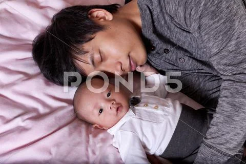 Restless infant baby boy with his sleeping father Stock Photos