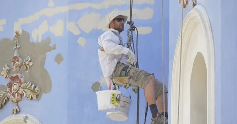 Restorer, Is Sitting on a Seat Holding on a Rope, Putting Down The Brush Into Stock Footage 52551353