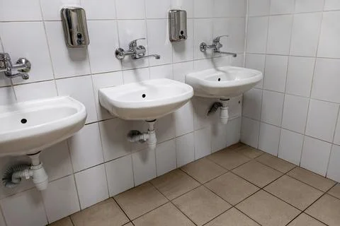 The restroom features three white sinks mounted on the wall. Each sink has a  Photos