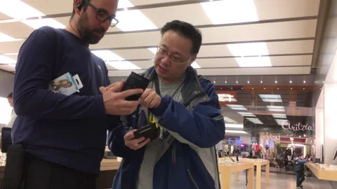 Retail Specialist Explaining Smartphone Features to a Customer in Electronics Stock Footage 343051404