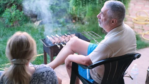 A retired couple is sitting in a backyard and frying a barbecue Video stock 244737680