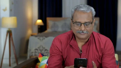 A retired Indian guy using a smartphone and posing for the camera - happy old... Stock Footage 202109684
