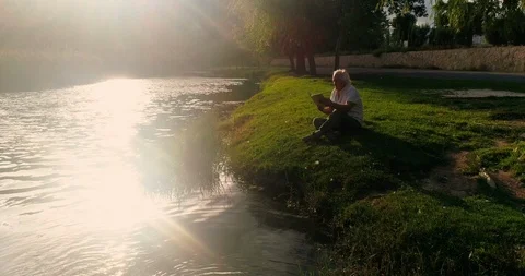 Retired lord reading in the field by the river Stock Footage 124381817