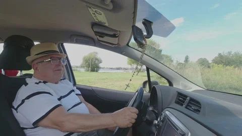 Retired man with glasses backs out automobile along meadow Stock Footage 140966769