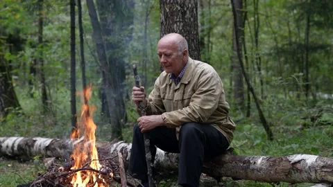 A retired man is resting by the campfire during a hike 스톡 동영상 168646695