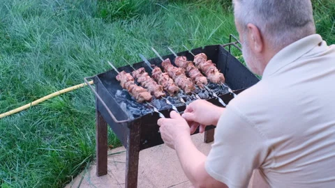A retired man is sitting in a backyard and frying a barbecue 스톡 동영상 244737660