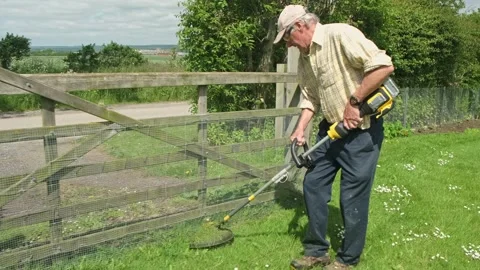 Retired man trimms the grass next to wooden garden gate in springtime Stock Footage 197128752
