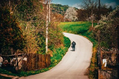Retired man walking through spring village on the asphalt road. He helps ours Stock Photos
