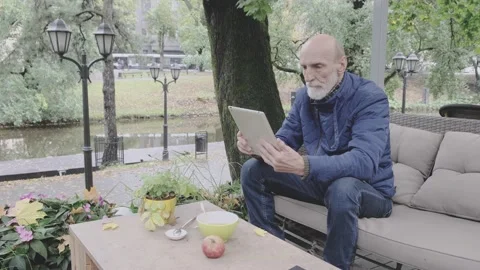Retired man wearing warm jacket sits in outdoor restaurant Stock Footage 146569766