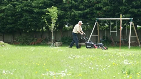 Retired middle aged man mowing the lawn in garden with swings and tree Stock Footage 197129610