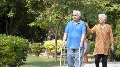 Retired old man doing a morning walk using a walker with his wife in a garden Stock Footage