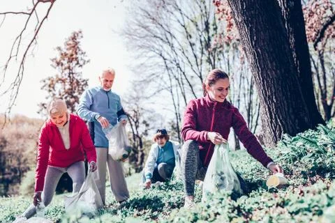 Retired people and young woman cleaning the forest together Stock Photos
