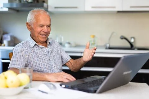 Retiree doing online shopping using laptop while sitting in the kitchen of home Stock-Fotos