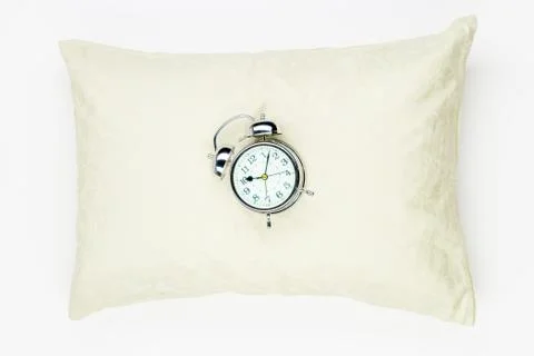 Retro alarm clock on the soft feather pillow close-up on a white background 스톡 사진