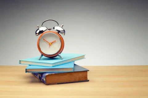 Retro alarm clock on stack of book over dark background for education and tim Stock Photos