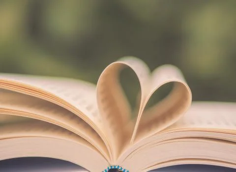Retro book on table in garden with top one opened and pages forming heart sha Stock Photos