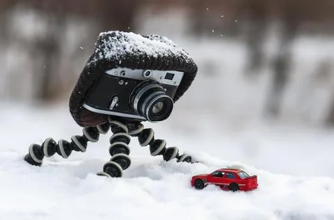 Retro camera with a hat is standing on a tripod on a winter blurred backgroun Stock Photos