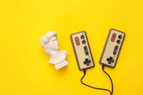 Retro gaming controllers with a bust sculpture on yellow background Stock Photos