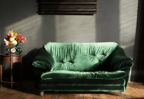 Retro interior featuring a plush green velvet sofa illuminated by soft sunlight Photos