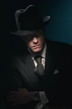 Retro mysterious gangster with hat in suit and tie. Against dark blue wall. Stock Photos