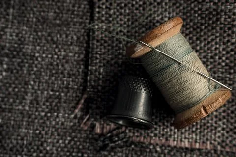 A retro needle with threads and an old thimble lie on a piece of cloth. Stock Photos
