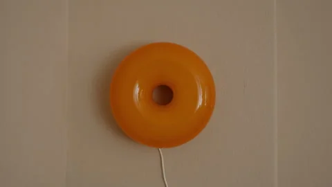 Retro orange glass ring wall lamp mounted on a plain beige wall in a flat Stock Footage 346144718