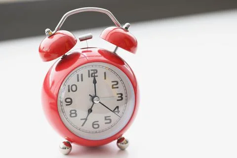 Retro red clock on white surface show seven in morning, wakeup, time for work Foto stock