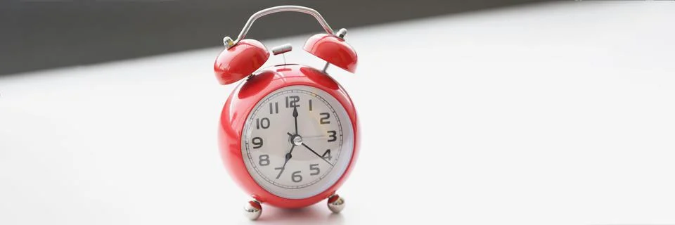 Retro red clock on white surface show seven in morning, wakeup, time for work Foto stock