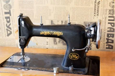 Retro sewing machine of Soviet production and old Soviet newspapers on the wall Stock Photos