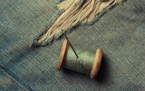 Retro skein thread with a needle on torn, rubbed jeans, sewing jeans, top vie Stock Photos
