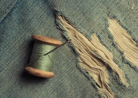 Retro skein thread with a needle on torn, rubbed jeans, sewing jeans, top vie Stock Photos