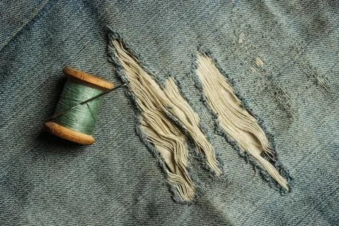 Retro skein thread with a needle on torn, rubbed jeans, sewing jeans, top vie 스톡 사진