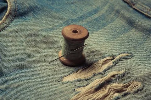 Retro skein thread with a needle on torn, rubbed jeans, sewing jeans, top vie Stock Photos