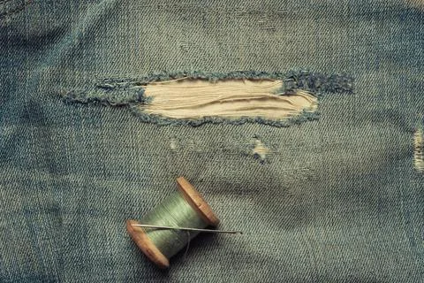 Retro skein thread with a needle on torn, rubbed jeans, sewing jeans, top vie Stock Photos