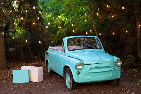 Retro small vintage car standing in garden on background garland burning bulbs. Stock Photos