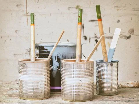 Retro styled image of used paint buckets and brushes in front of a stained wa Stock Photos