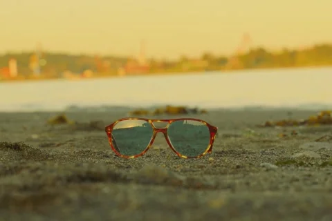 Retro tortoise shell aviator sunglasses on beach at sunset Stock-Footage 332399574