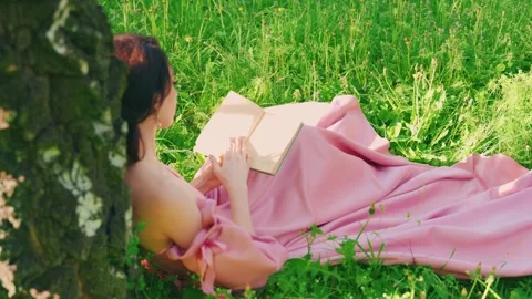 Retro woman sitting under tree reading paper book. Summer garden green grass Stock Footage 308094450