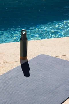 Reusable bottle is standing on stone pool deck near pool edge, casting long Foto stock