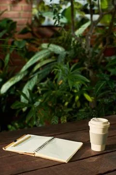 Reusable Coffee Cup with Blank Notebook in Green Garden Workspace Fotos de archivo
