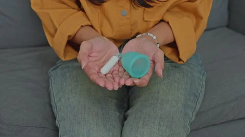 Reusable menstrual cup and white cotton tampon held in hands for feminine Stock Footage 340576301